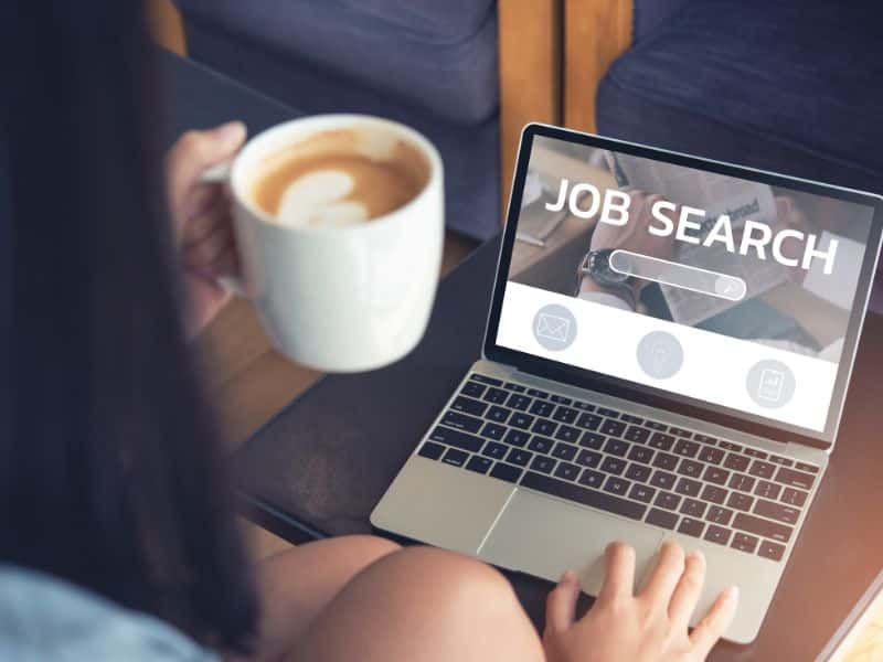 A candidate uses AI in her job search, working on her laptop with a coffee in hand.