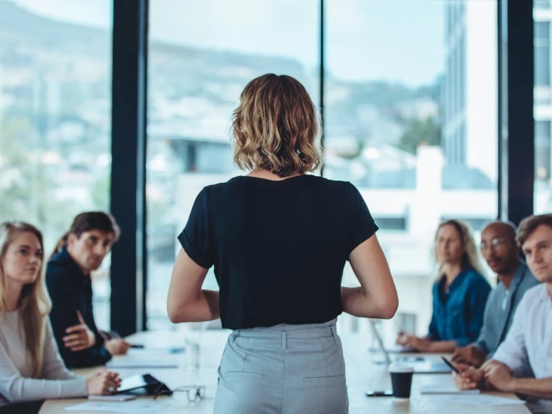 A fractional leader leads a meeting in front of a group of professionals sitting at a conference table
