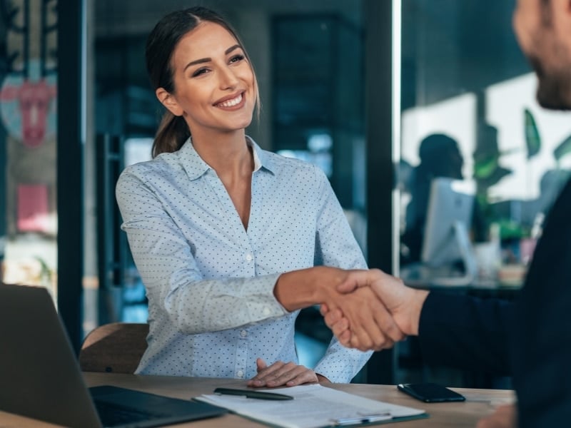 A woman shakes the hand of a HR leader while interviewing for a position, highlighting the candidate experience in an interview.