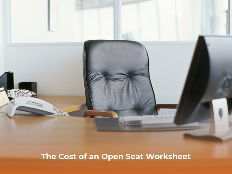 A professional business desk sits empty, showing an empty chair, desk, computer, and phone, representing an unfilled position.